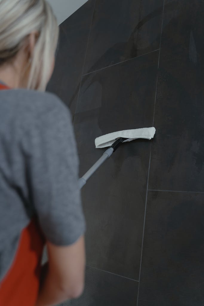 Close-up of a woman cleaning a dark wall with a mop, highlighting modern home cleaning methods.