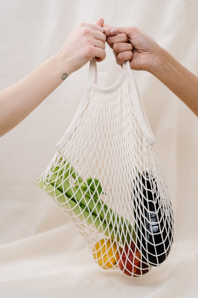 Hands holding a mesh bag filled with fresh vegetables, promoting sustainable shopping practices.